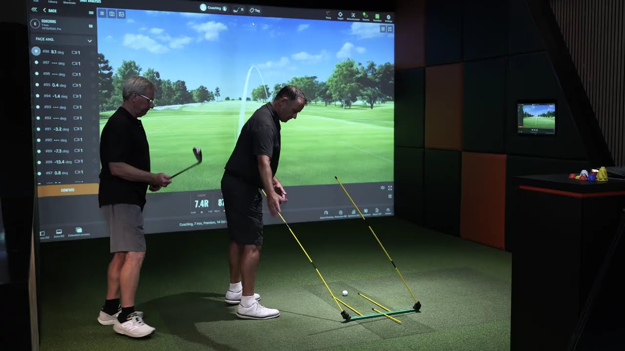 Coach and golfer in simulator discussing swing technique with Stryper SwingMate on ground