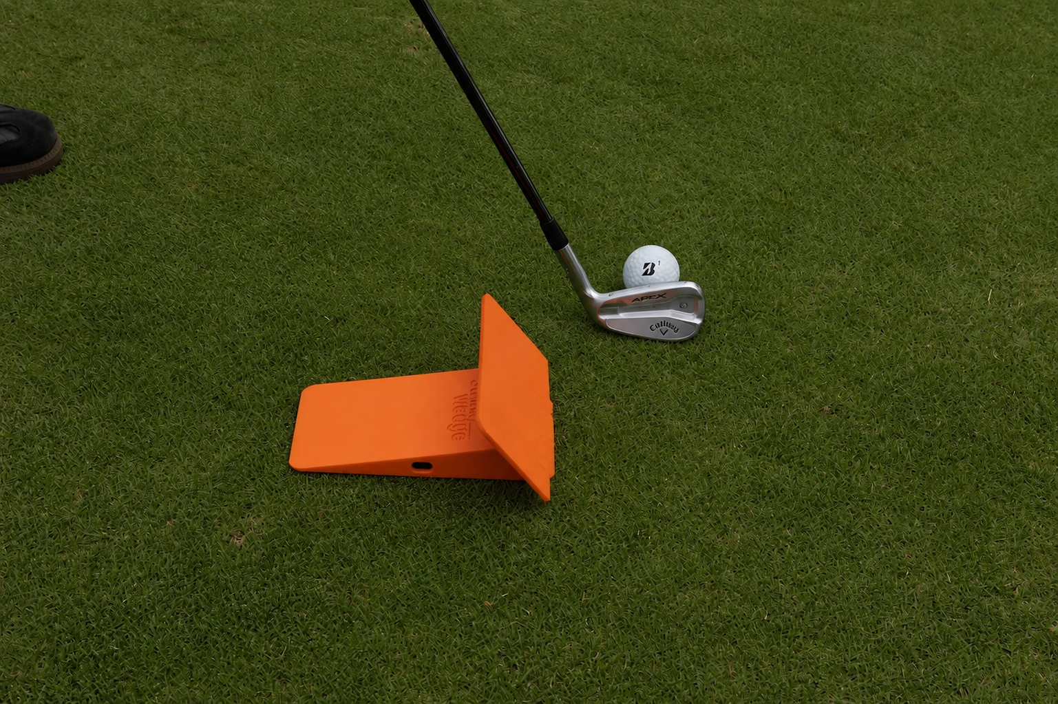 Strike Wedge training block positioned next to a golf ball and iron in setup position